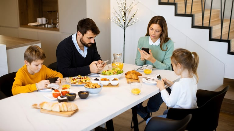 Estar conectados al teléfono hace que nos perdamos de una linda comida familiar (Foto: Adobe Stock)